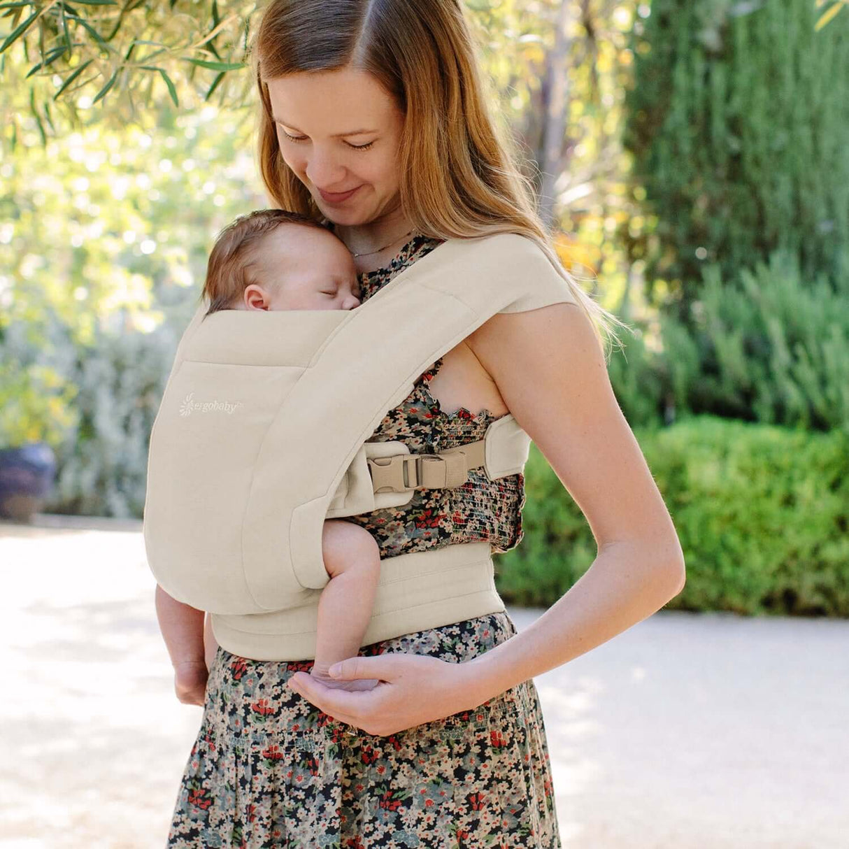 A mother lovingly carries her sleeping baby in the Ergobaby Embrace, Cosy Carrier - Cream, featuring ergonomic design | Babymaxi