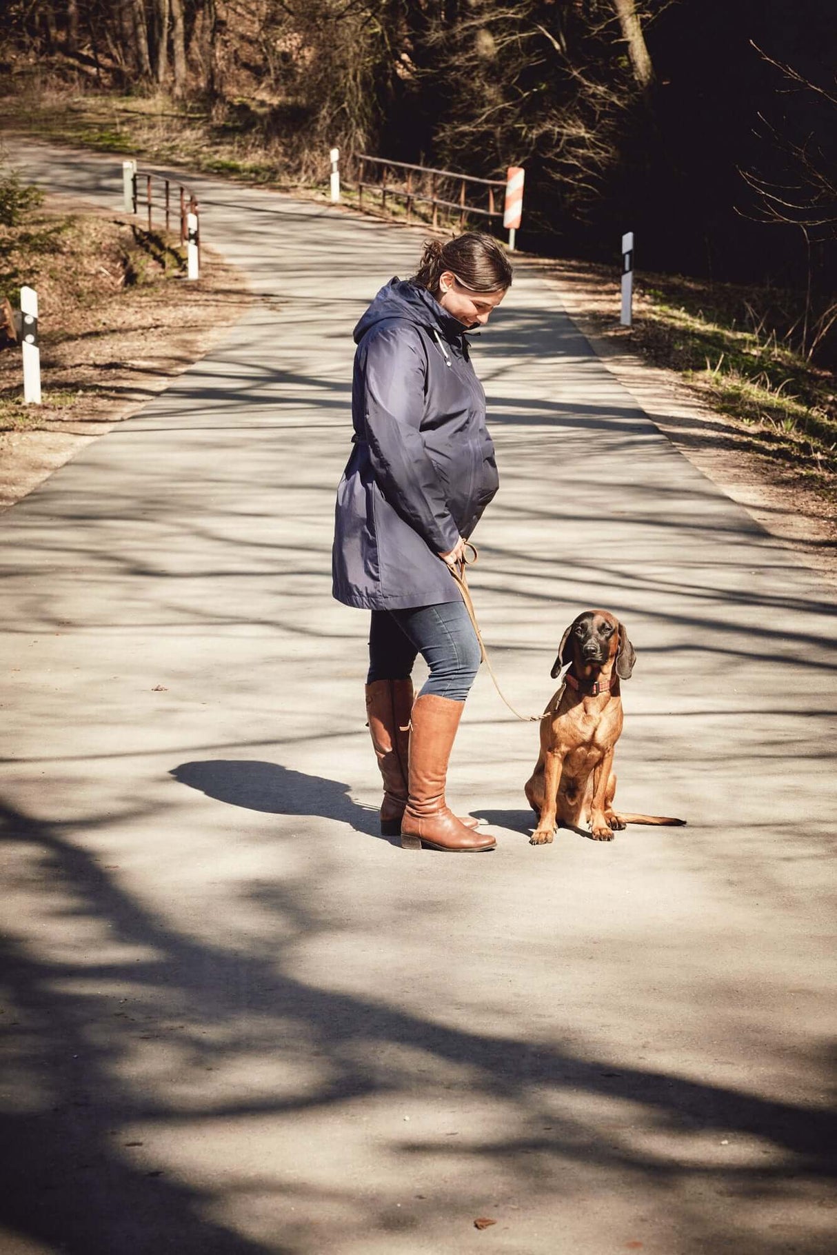 Woman wearing Mamalila Dublin Babywearing Coat – Navy walking her dog on a sunny path | Babymaxi
