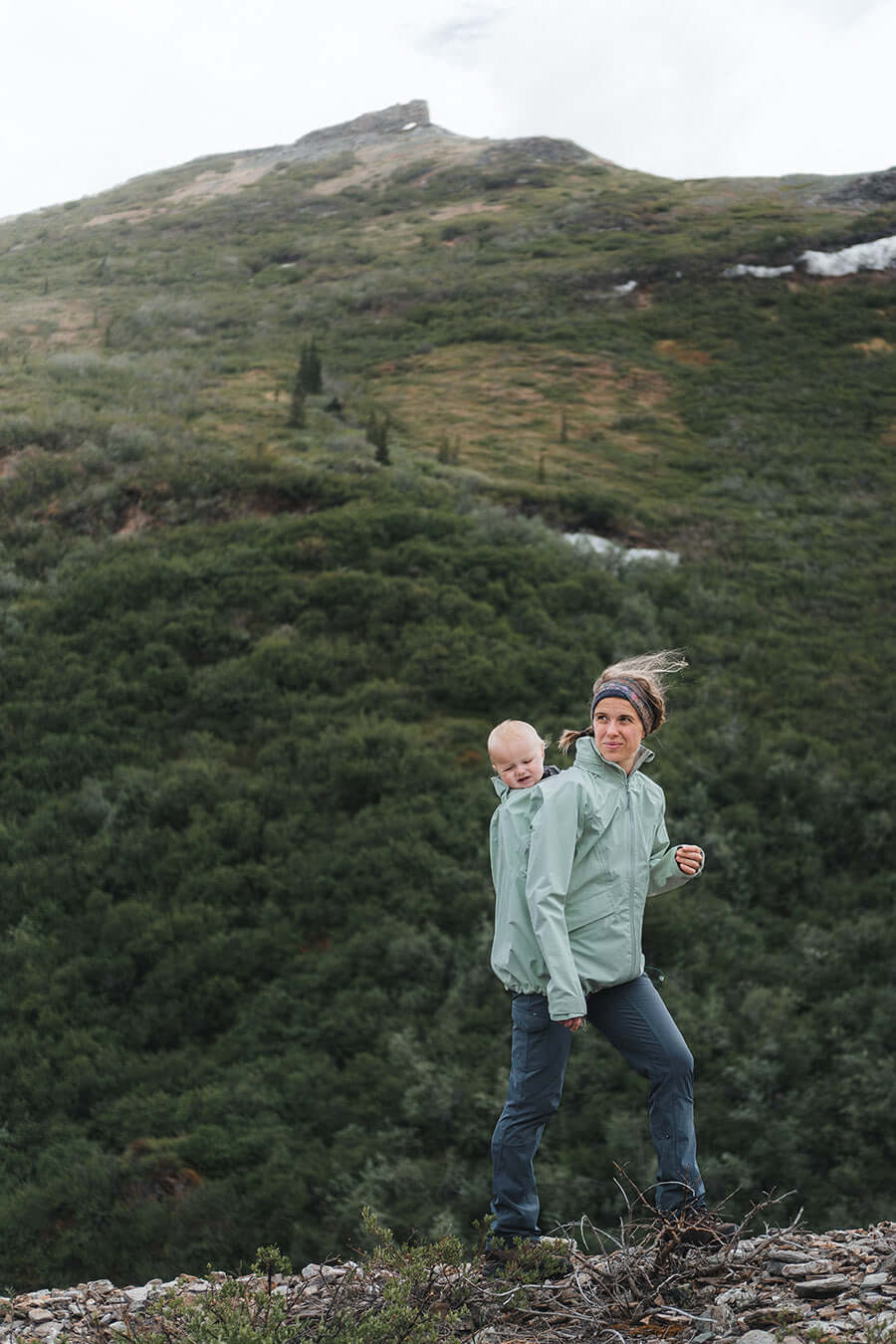 Mamalila Explorer Outdoor Baby Carrier Jacket - Mint worn by a mother with baby in a carrier against a green mountain backdrop | Babymaxi