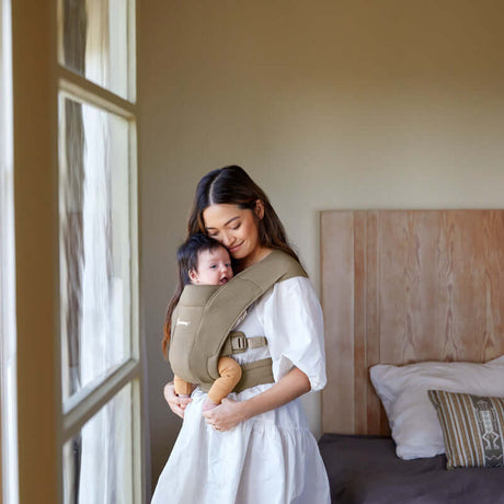 Mom carrying baby in Ergobaby Embrace - Soft Olive carrier, showcasing comfort and ergonomic design | Babymaxi