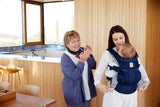 Mom using Ergobaby Omni Breeze - Midnight Blue baby carrier with smiling grandmother in modern kitchen | Babymaxi