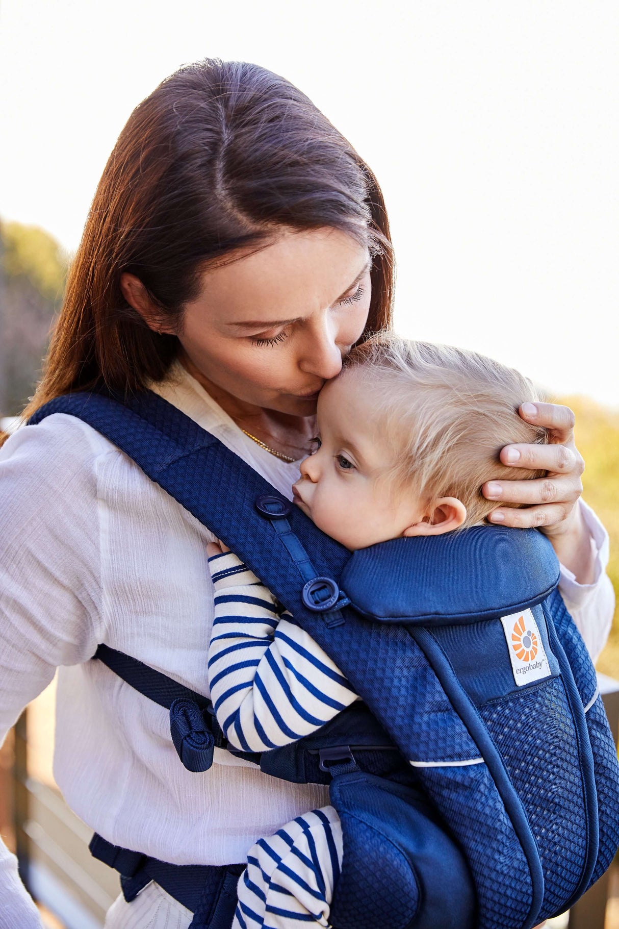 Mom kissing baby in Ergobaby Omni Breeze - Midnight Blue carrier, featuring breathable SoftFlex Mesh for comfort | Babymaxi