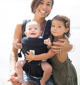 Mother using Ergobaby Omni Classic Cotton Carrier - Pure Black with baby, smiling toddler beside her | Babymaxi