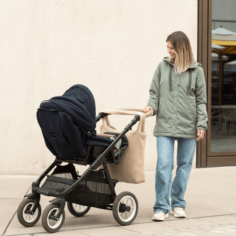 Mamalila Boston Babywearing Jacket - Agave worn by a woman next to a stroller, perfect for mother and baby on-the-go | Babymaxi