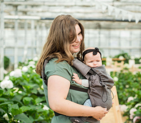 Mom joyfully carrying baby in Neko Switch Baby Carrier - Bold, 2 extra hoods in a lush garden setting | Babymaxi