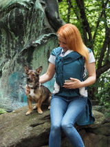 Woman wearing Storchenwiege Bondima Wrap Baby Carrier - Turquoise while sitting with a dog in a natural setting | Babymaxi