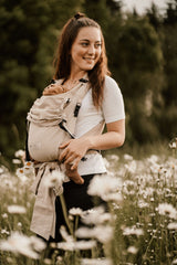 Woman wearing Storchenwiege Talemo Half-Buckle Baby Carrier - Natural with baby in flower field | Babymaxi