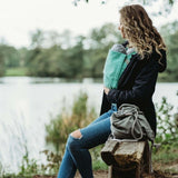 Woman wearing Wombat & Co. London - Wallaby Maternity & Babywearing Coat - Navy while babywearing by a lake | Babymaxi