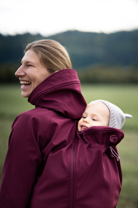 Mamalila Softshell Babywearing Jacket Allrounder Fit Burgundy, laughing mom carrying baby on her back outdoors